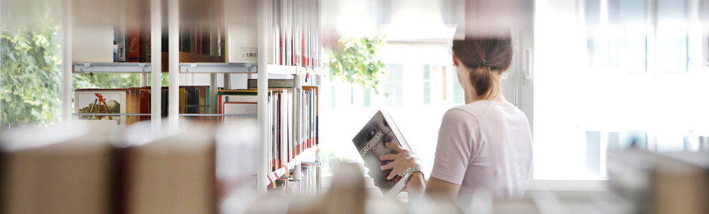 Frau, die zwischen Bücherregalen steht. 