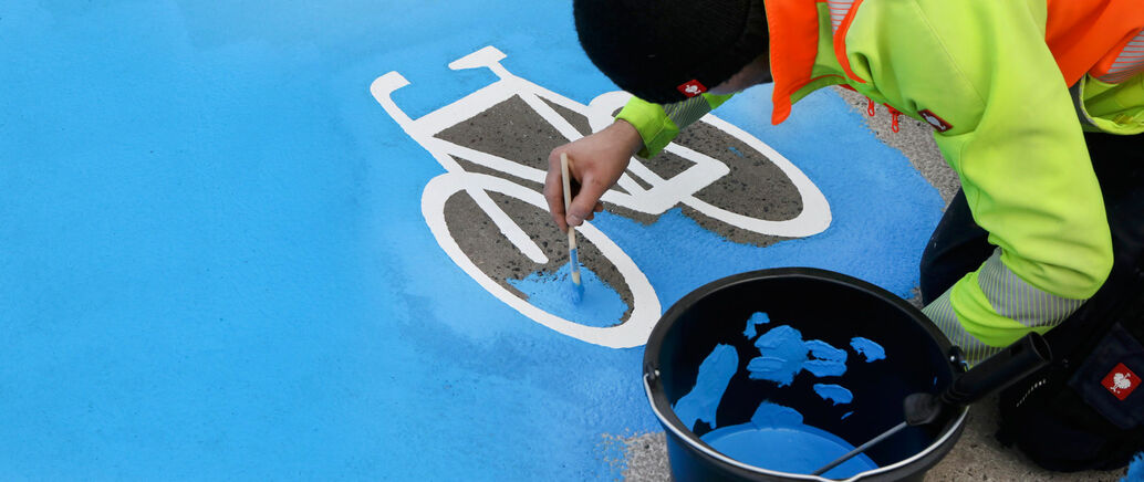 Person, die die Straße mit blauer Farbe als Fahrradstreifen markiert