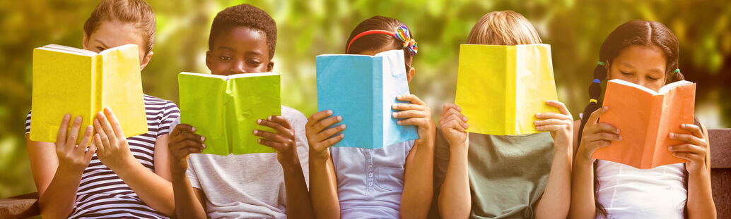 Mehrere Kinder, die nebeneinander sitzen und ein Buch in ihren Händen halten.