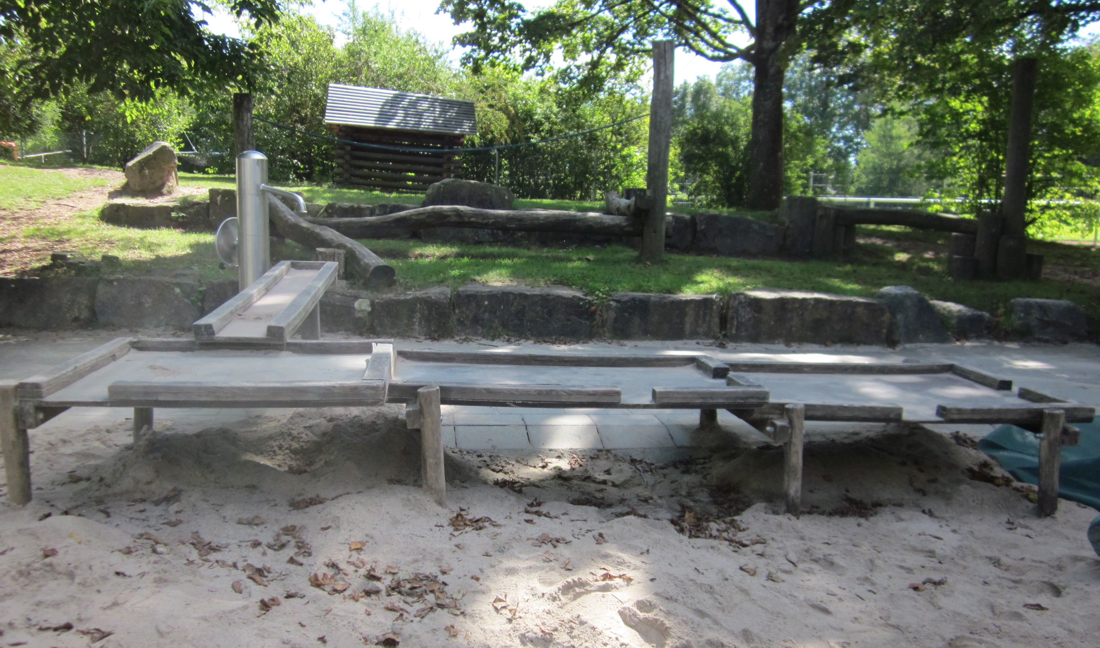 Das Bild zeigt den Sandkasten mit Matschtisch und Wasserpumpe.