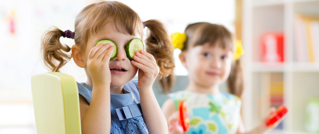 Zwei Kinder, eines hält sich Gurkenscheiben vor die Augen