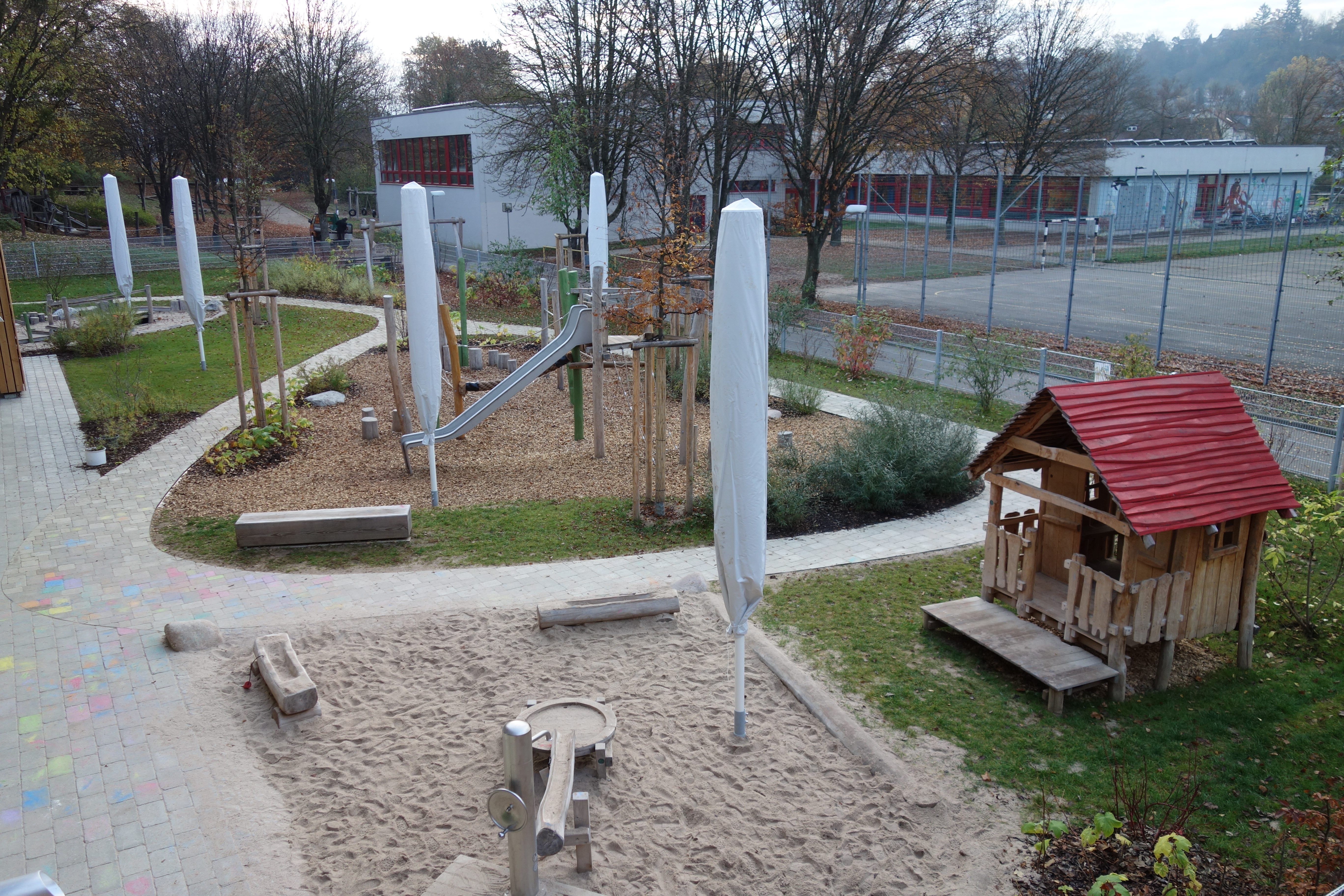 Das Bild zeigt den Garten aus erhöhter Position fotografiert. Im Vordergrund ist ein Sandkasten mit Spielhaus zu erkennen. Im Hintergrund steht ein Klettergerüst mit Rutsche.