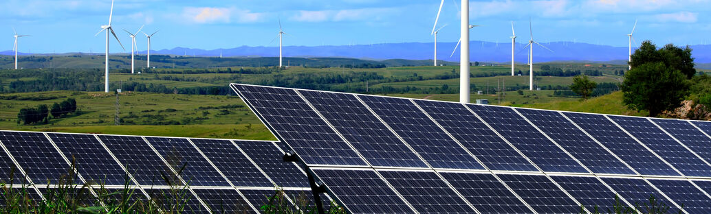 Landschaftsaufnahme mit Photovoltaikanlagen im Vorder- und Windrädern im Hintergrund 