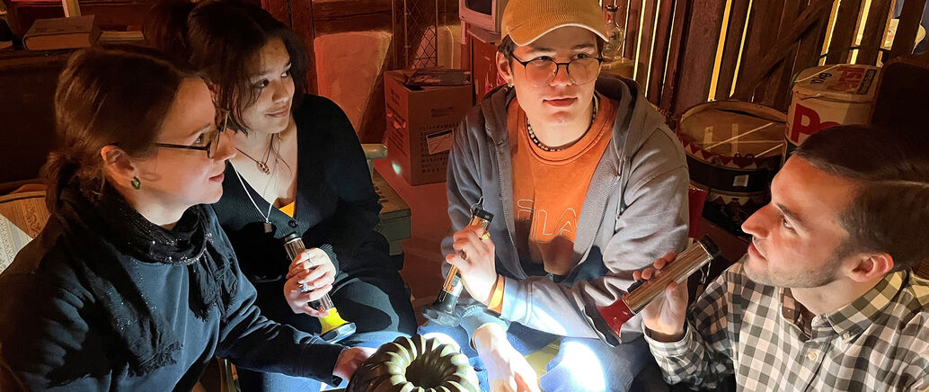 Vier junge Menschen sitzen mit einer Taschenlampe im Halbkreis. 