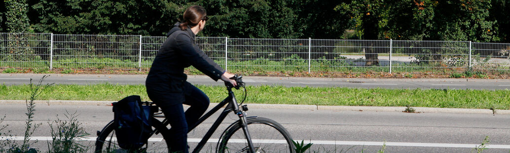 Eine Frau fährt auf dem Fahrrad an Bäumen vorbei.