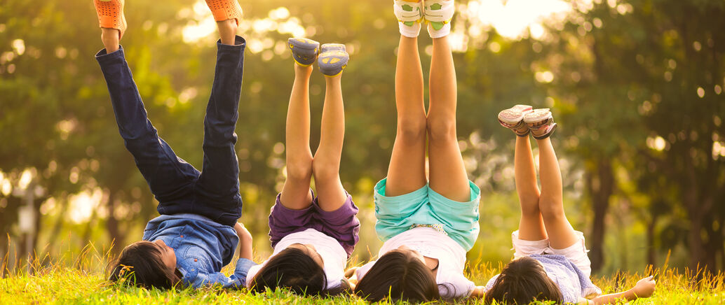 Kinder liegen auf einer Wiese und strecken die Füße in die Höhe