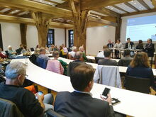 Menschen sitzen im Ratsaal im Rathaus und schauen auf eine Beamerleinwand