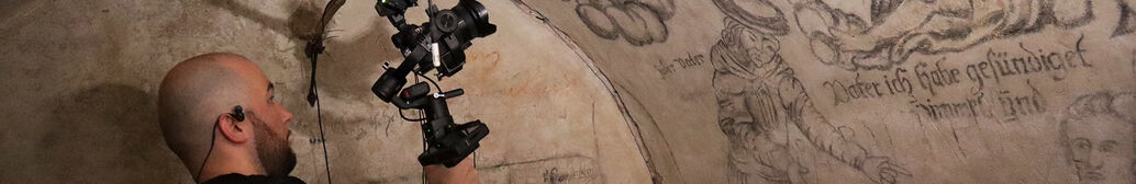 Ein Mann steht im Karzer in der M&uuml;nzgasse und h&auml;lt eine Kamera. Damit macht er Aufnahmen von den bemalten W&auml;nden.