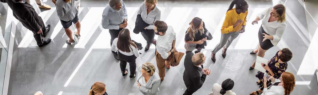 Gesch&auml;ftsleute stehen in mehreren Gr&uuml;ppchen und unterhalten sich.