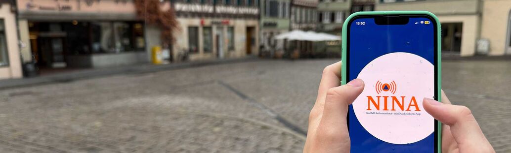 Warn-App Nina auf dem Handy vor der Kulisse des T&uuml;binger Marktplatzes