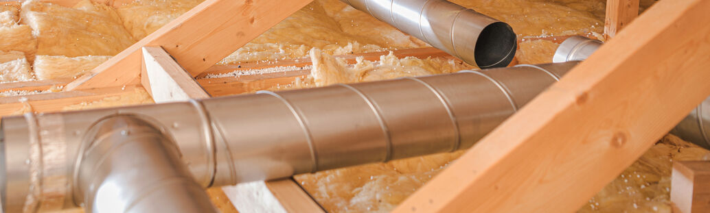 silberne Rohre zwischen Holzbalken und D&auml;mmmaterial