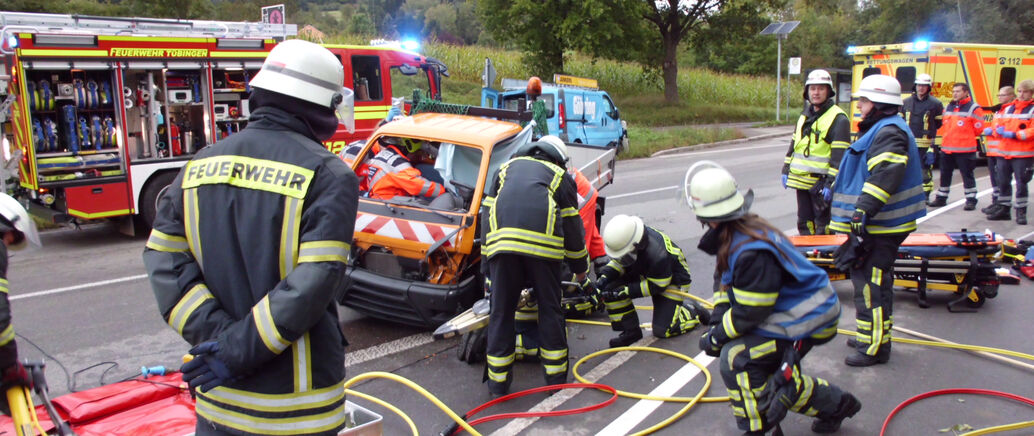 Feuerwehrm&auml;nner sind bei einem Verkehrsunfall im Einsatz. Sie untersuchen ein kaputtes Auto.