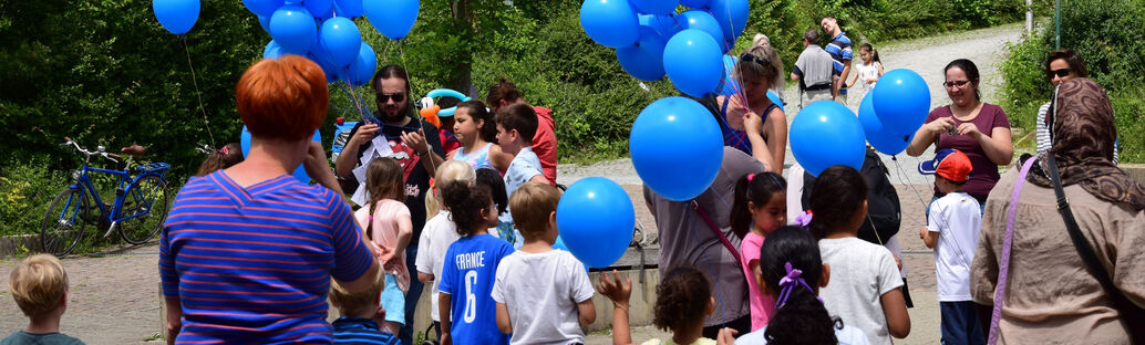 Eine Gruppe von Menschen l&auml;sst blaue Luftballone steigen.