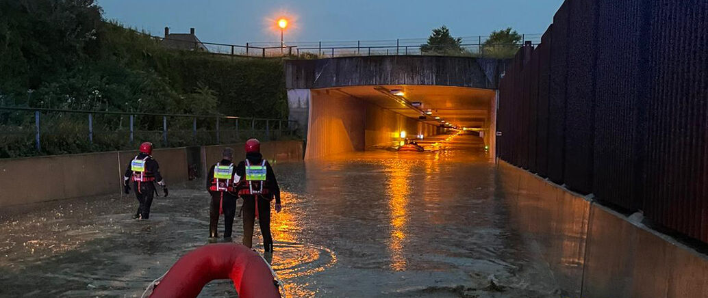 Feuerwehrm&auml;nner stehen vor einem Tunnel, der nach einem Unwetter &uuml;berflutet ist.