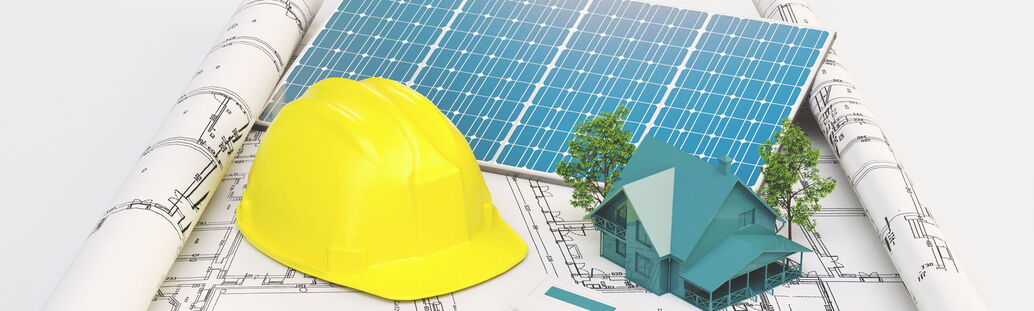 Geb&auml;udeplan, auf dem ein Solarmodul, ein Bauhelm, ein Modelhaus und ein Taschenrechner liegen