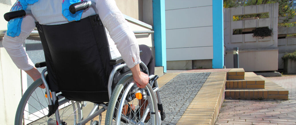 Frau im Rollstuhl die eine Rampe hochfährt